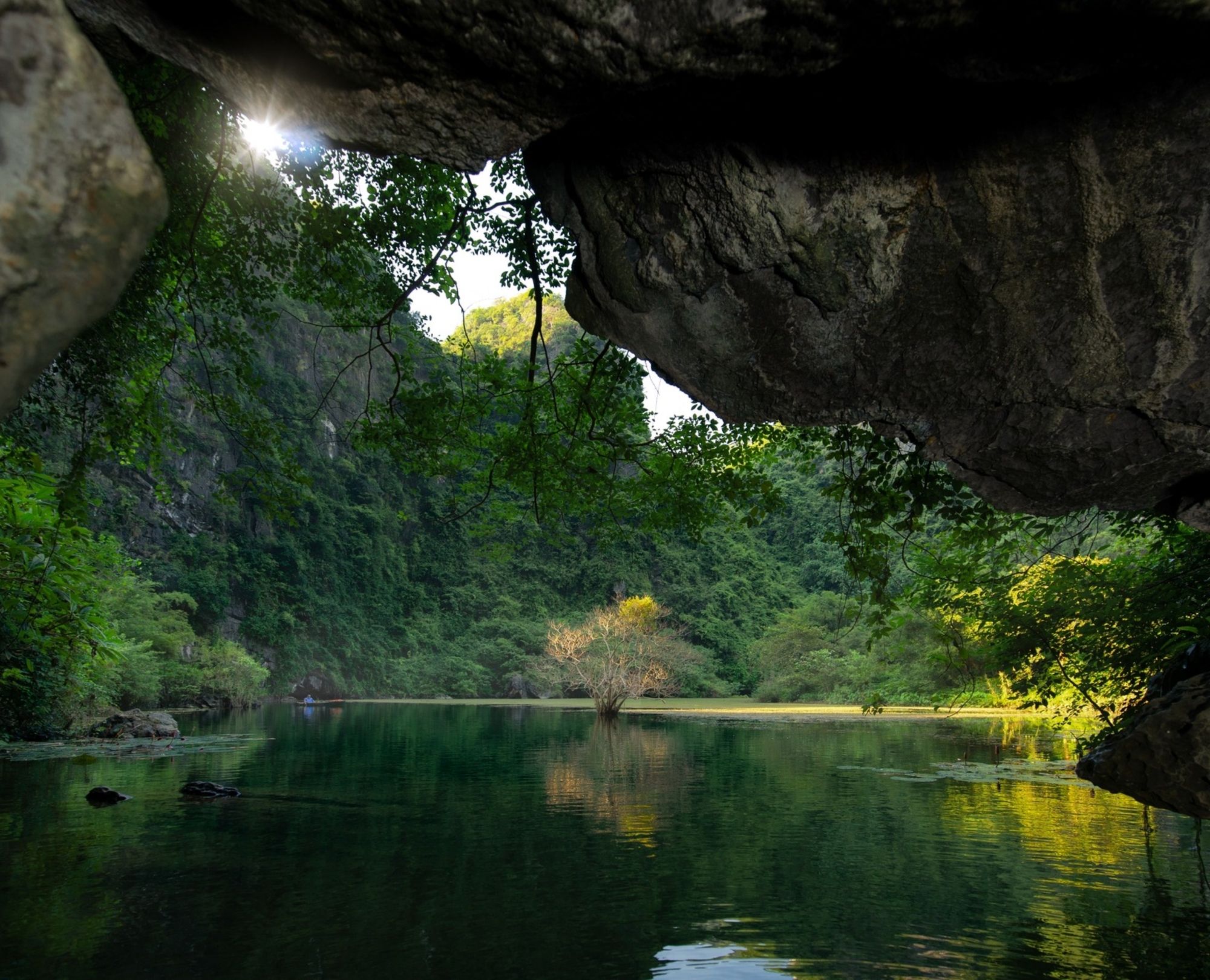A stunning view from inside a limestone cave looking out towards the emerald waters and lush green mountains of Trang An, Ninh Binh